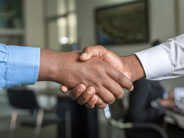 Close-up of two professionals shaking hands in an office setting, symbolizing partnership and trust for Town Listing Guide